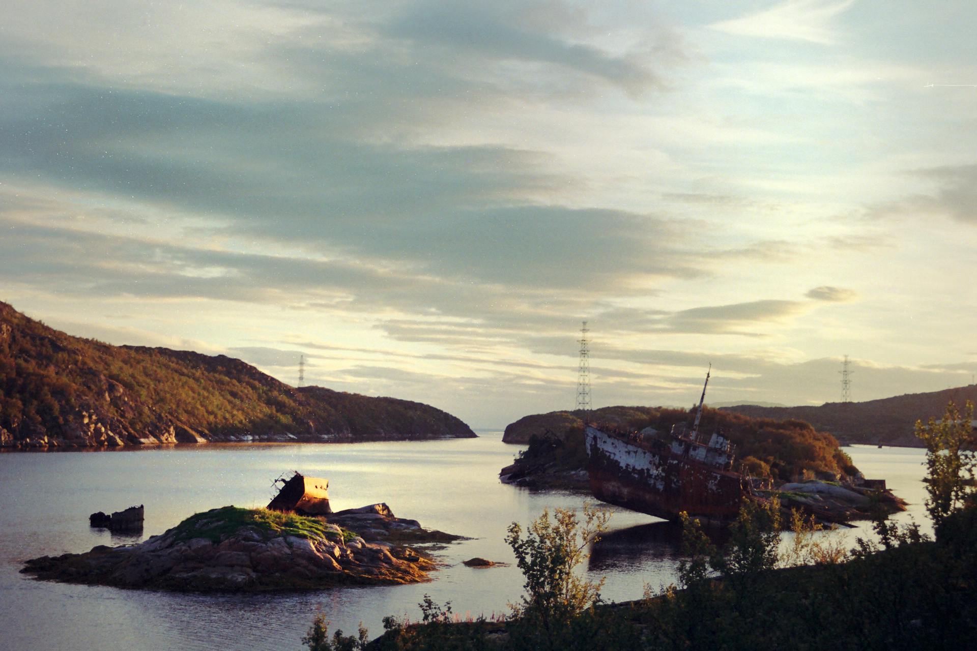 A serene landscape view of a shipwreck on a distant island at sunset.