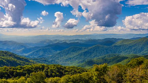 Free Breathtaking aerial view of rolling green mountains under a vibrant blue sky with fluffy clouds. Stock Photo