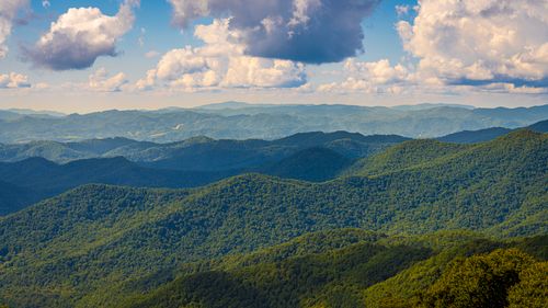 Free Vast mountain range with lush greenery under a bright blue sky featuring fluffy clouds. Stock Photo