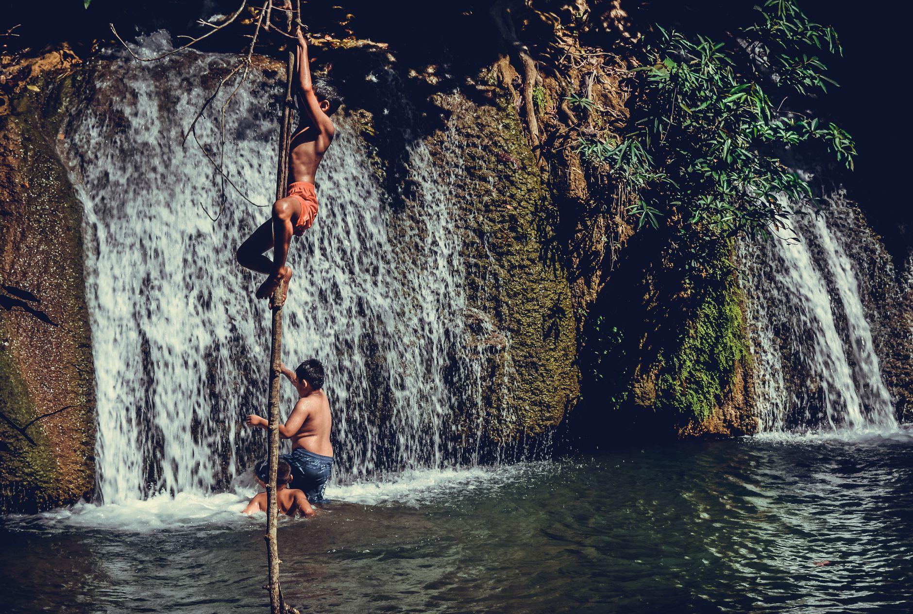 Boys enjoying a summer day climbing near a waterfall in Thailand.