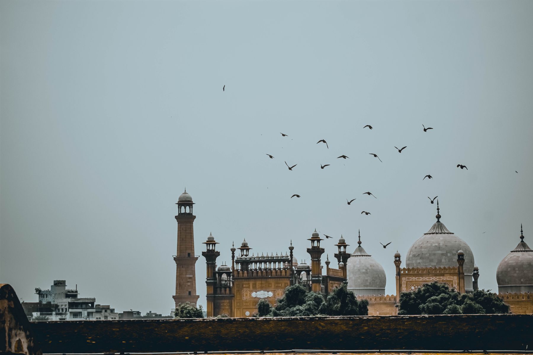 Scenic view of Badshahi Mosque in Lahore with flying birds against a clear blue sky.