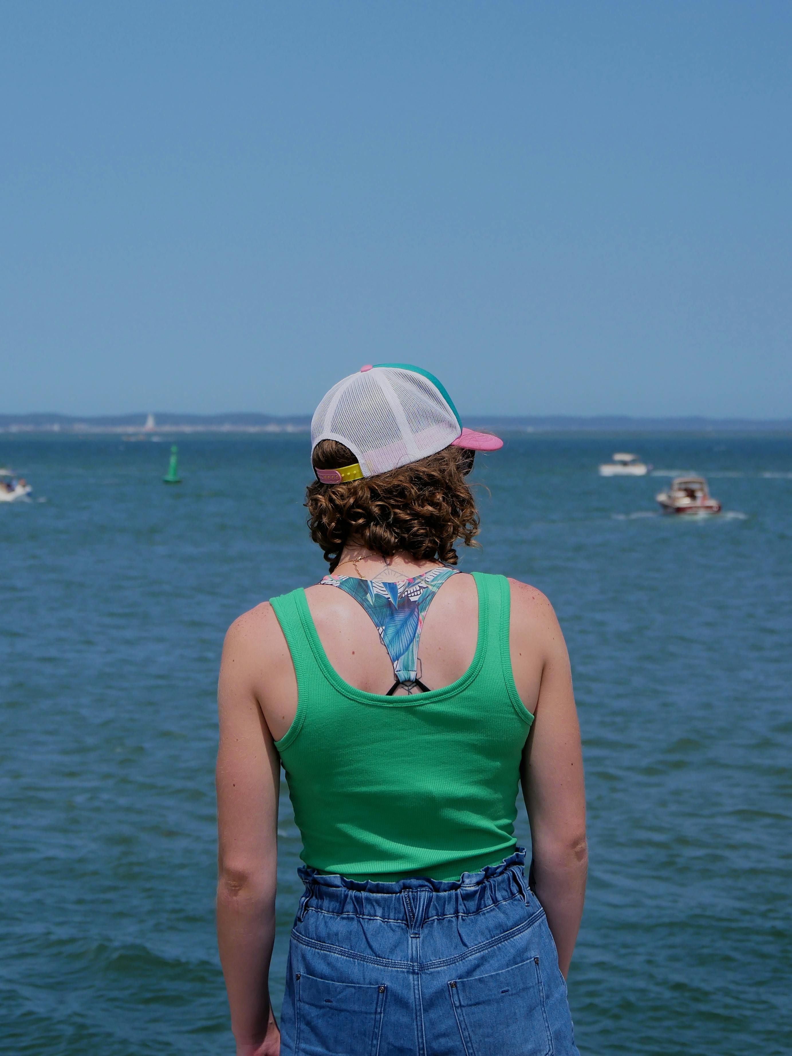 Back view of a woman in a cap and green top overlooking the sea in Arcachon, France.