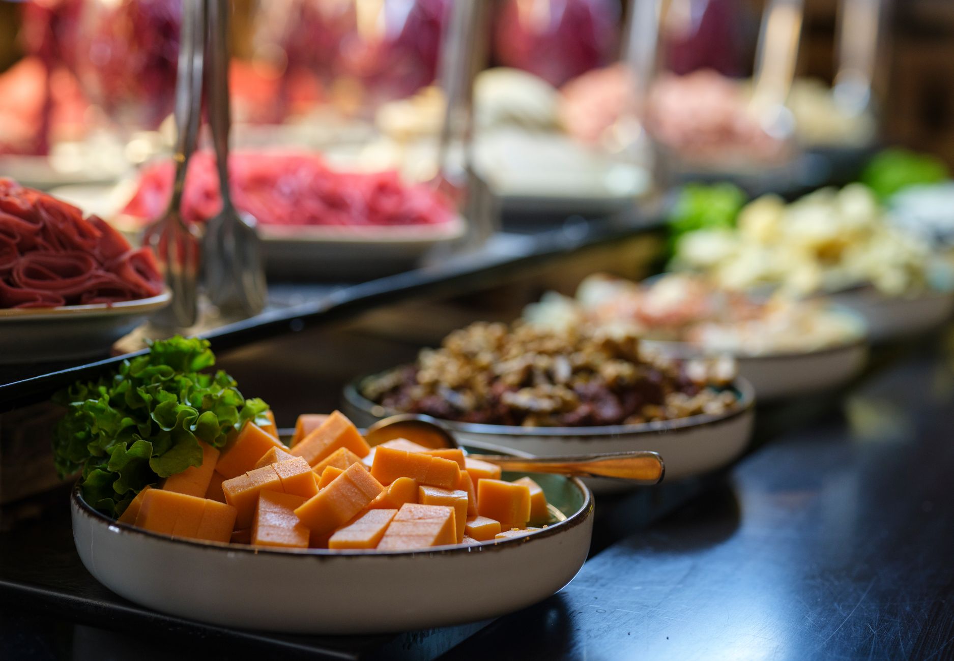 Wide view of a delicious vegetarian buffet featuring fresh ingredients like cheese, lettuce, and nuts in ceramic bowls.