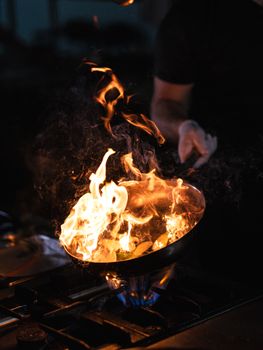 A chef skillfully maneuvers a pan engulfed in vibrant flames on a stove.
