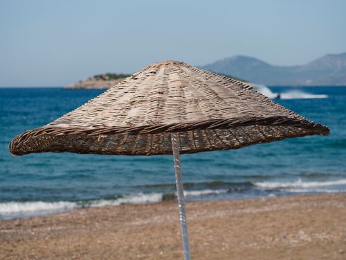 Free A picturesque beach scene featuring a wicker sunshade against a blue sea backdrop. Stock Photo