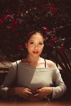Elegant woman in gray top with red floral backdrop, captured during the day.