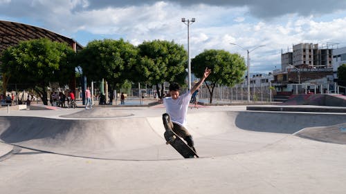 Man in White T-shirt and Black Pants Doing Skateboard Stunts on Gray Concrete Ramp