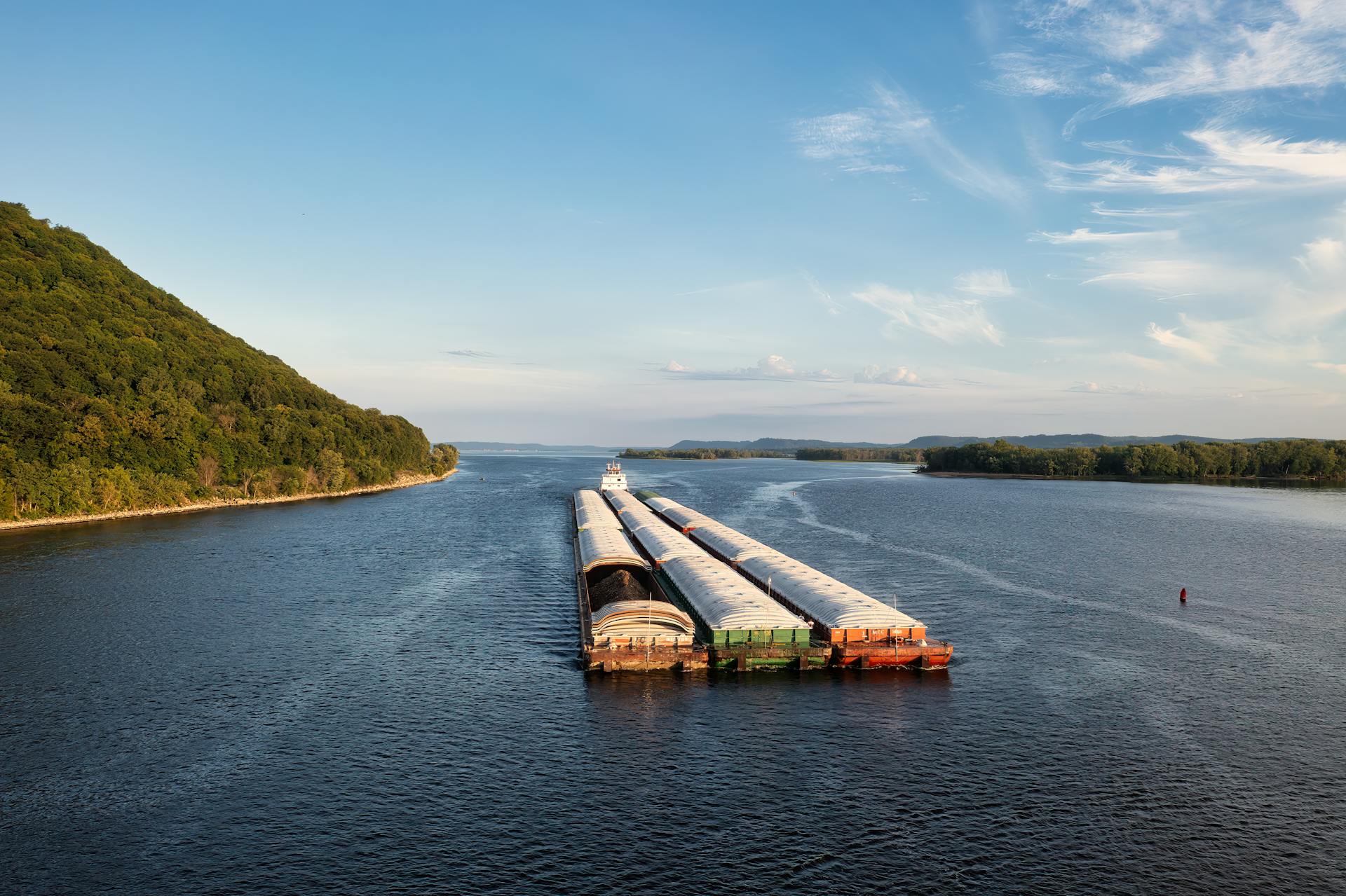 A barge navigates the Mississippi River near Reads Landing, MN, framed by lush greenery under a clear sky.