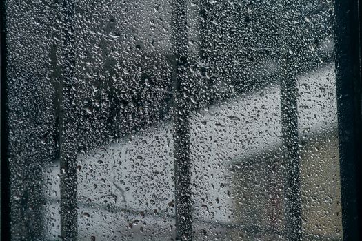 Close-up of rain-soaked window with water droplets, creating a moody and cool atmosphere.