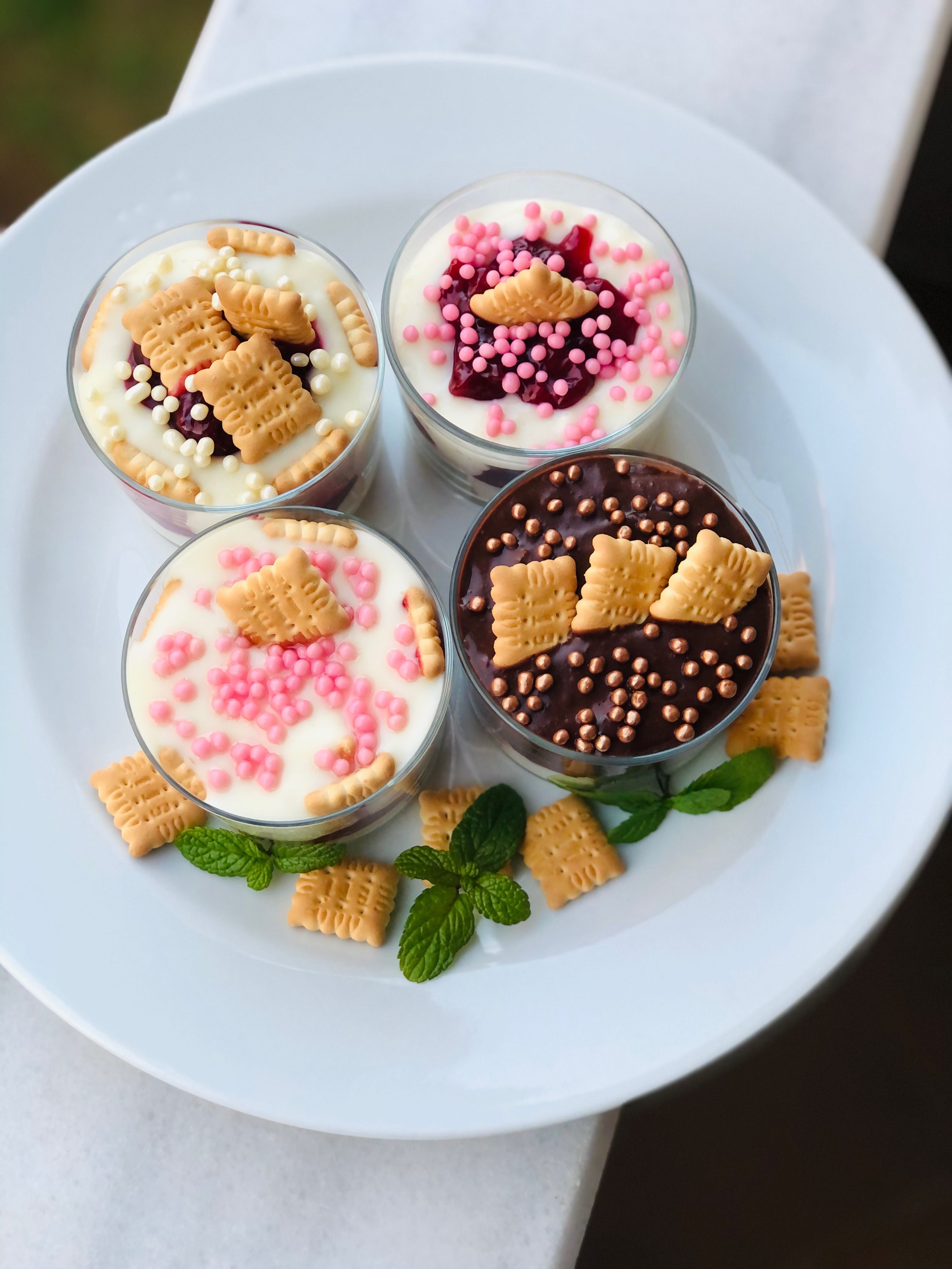 Delicious dessert cups adorned with colorful sprinkles and biscuit toppings, served on a white plate.