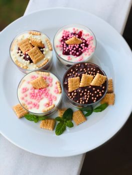 Delicious dessert cups adorned with colorful sprinkles and biscuit toppings, served on a white plate.