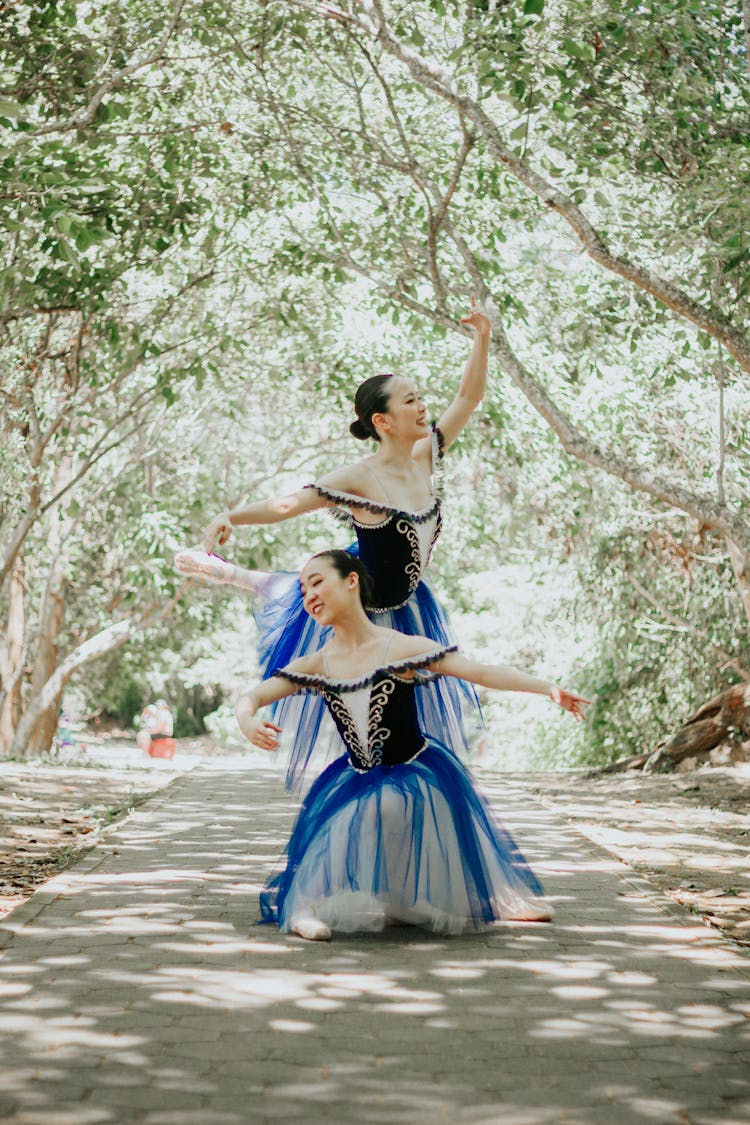 Beautiful Ballerinas Dancing On The Street Between Green Trees
