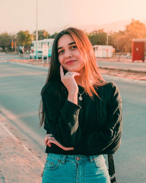 Free A young woman poses confidently on a sunny street, dressed casually in a black sweater and denim jeans. Stock Photo