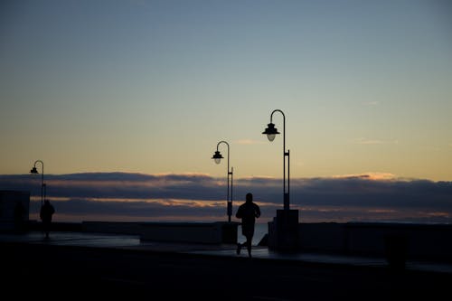 Silhouette of Man Running on Boardwalk on Sunset