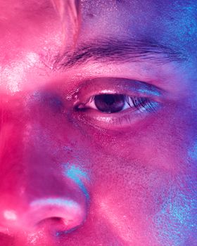 Close-up portrait of an eye illuminated by vibrant neon lights, showcasing skin texture and color contrasts.