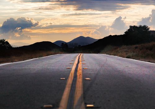 Free A scenic road leading towards mountains is framed by a dramatic sunset sky. Stock Photo