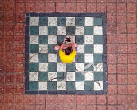 Aerial shot of a man controlling a drone on a checkerboard pattern patio in Indonesia.