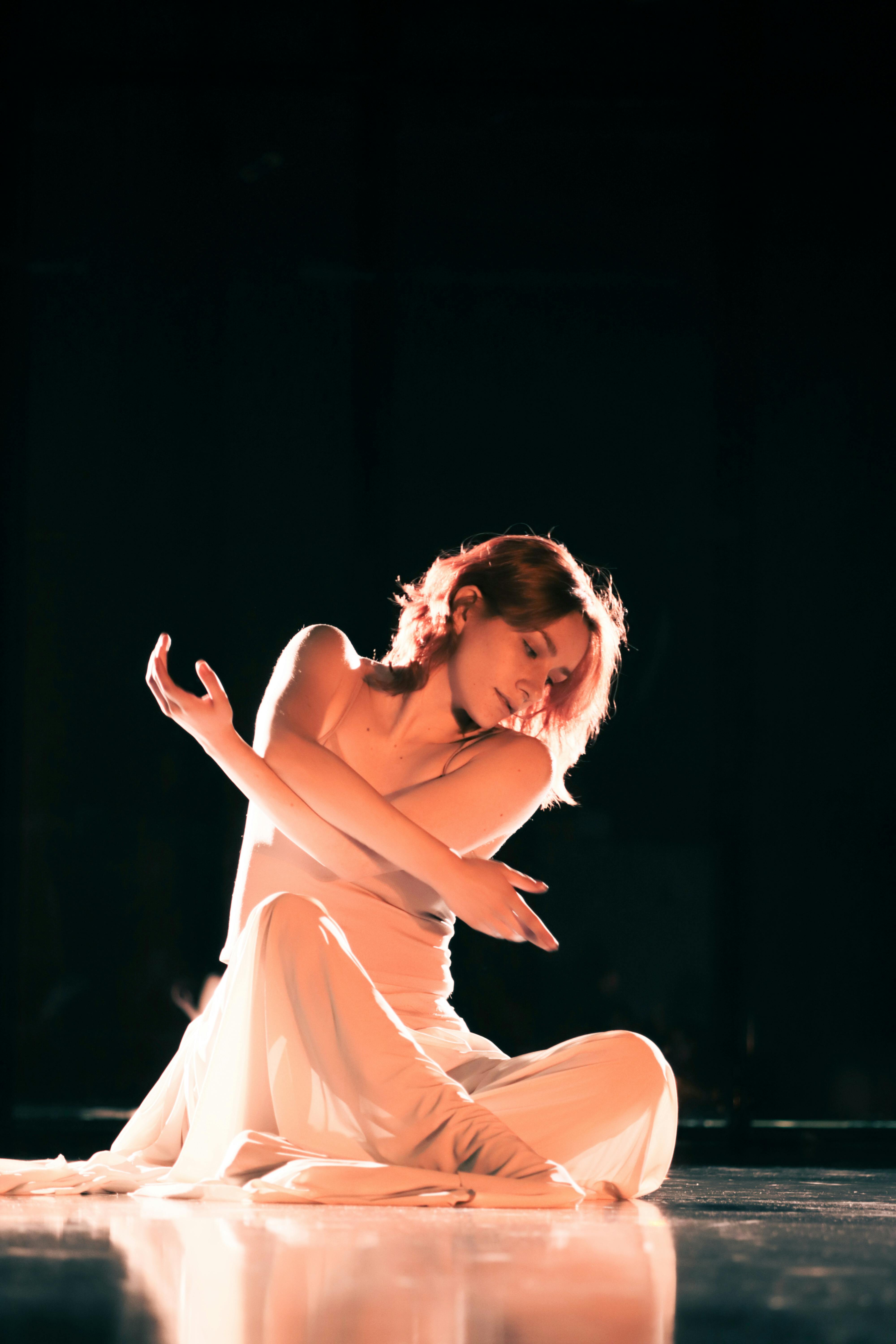 Free A woman in a flowing gown performs an expressive dance on a dimly lit stage. Stock Photo