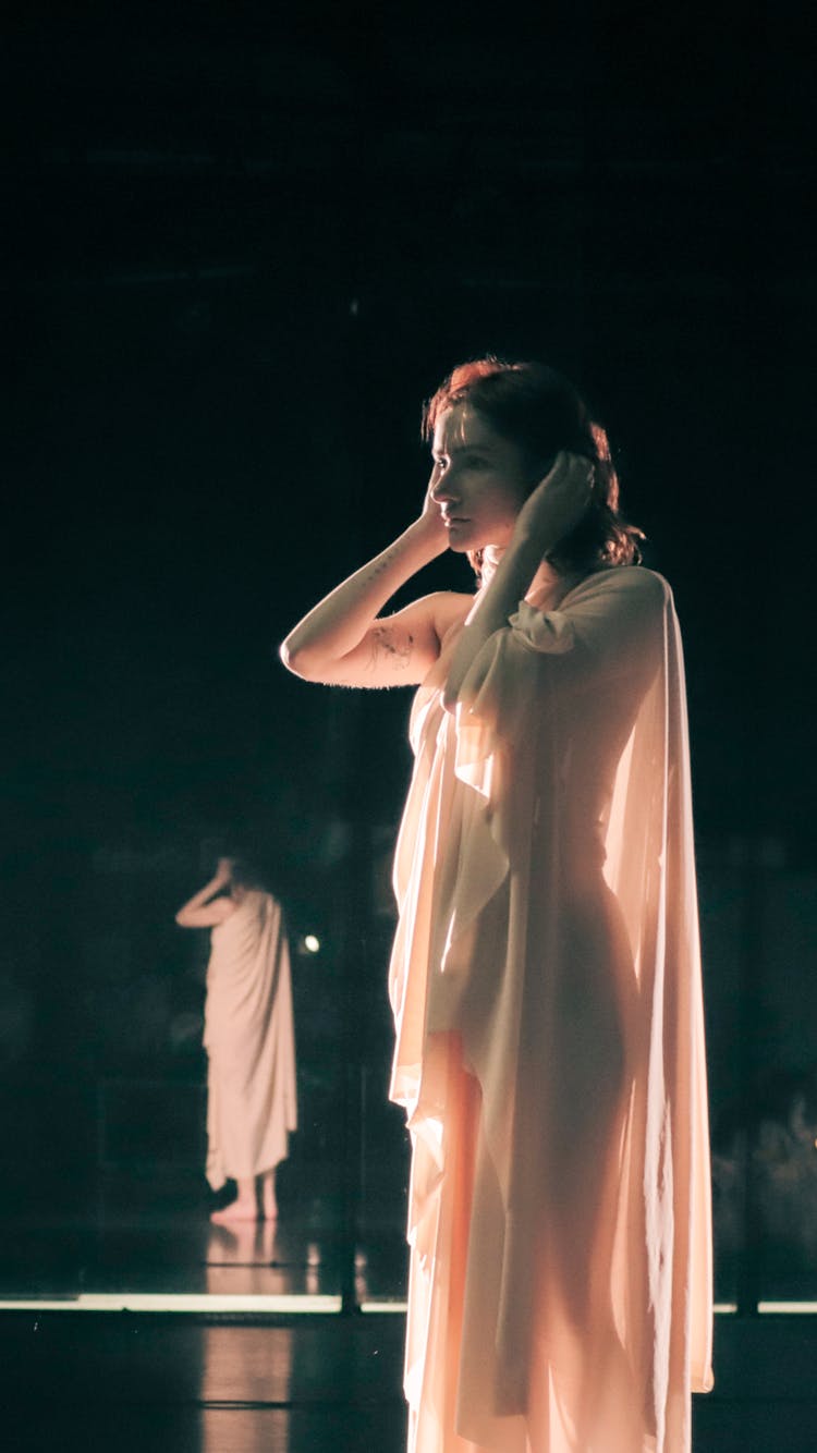 Actors Standing On A Dark Stage, Wearing Illuminated Flowing Tunics