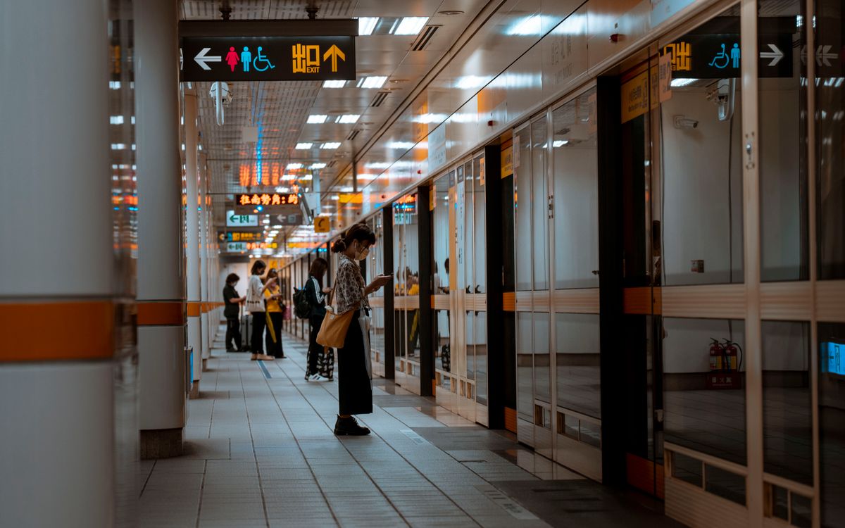 A bustling subway corridor with people standing and waiting near directional signs.