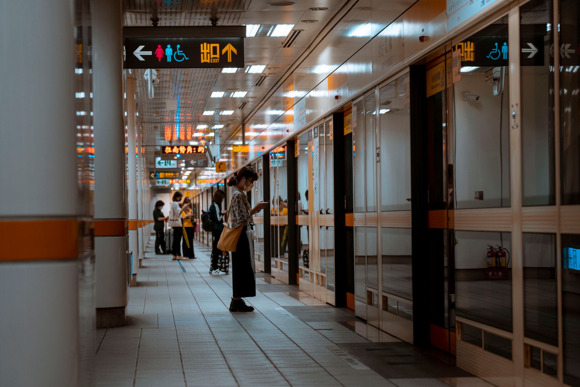 Um corredor movimentado do metrô com pessoas em pé, aguardando perto de placas indicativas.