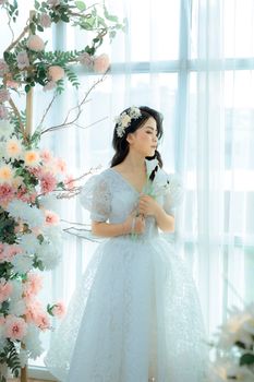 Beautiful woman in lace dress holding flowers with eyes closed, posing gracefully indoors.