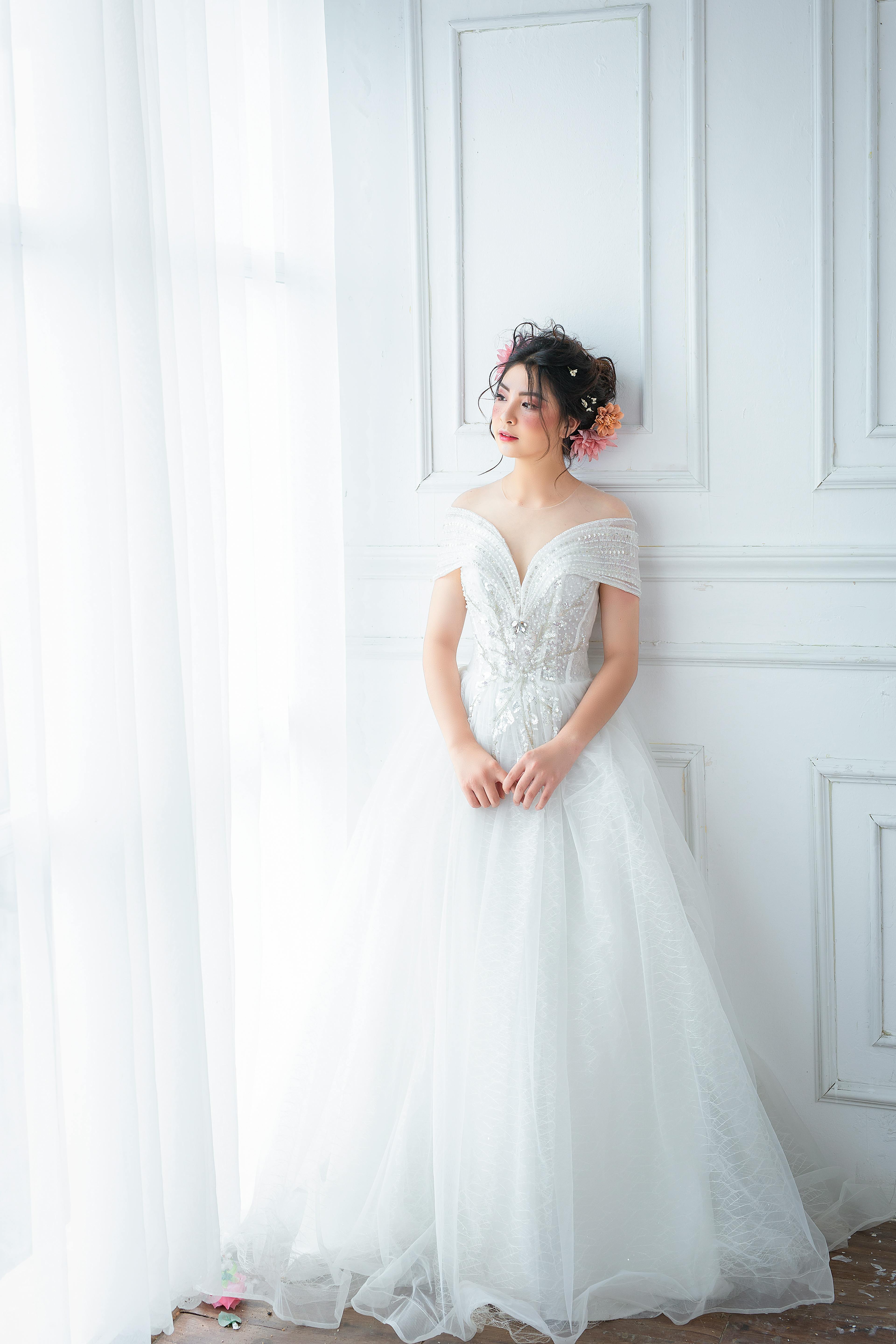 Elegant bride in white gown near window with natural light.