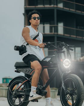 A young man sitting on an electric bicycle wearing sunglasses, captured during the day outdoors.