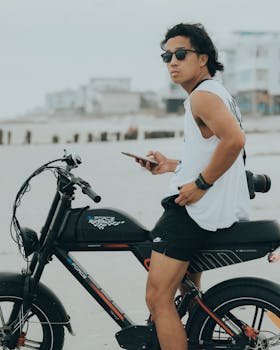Asian man on electric bike using smartphone at Miami beach in summer.