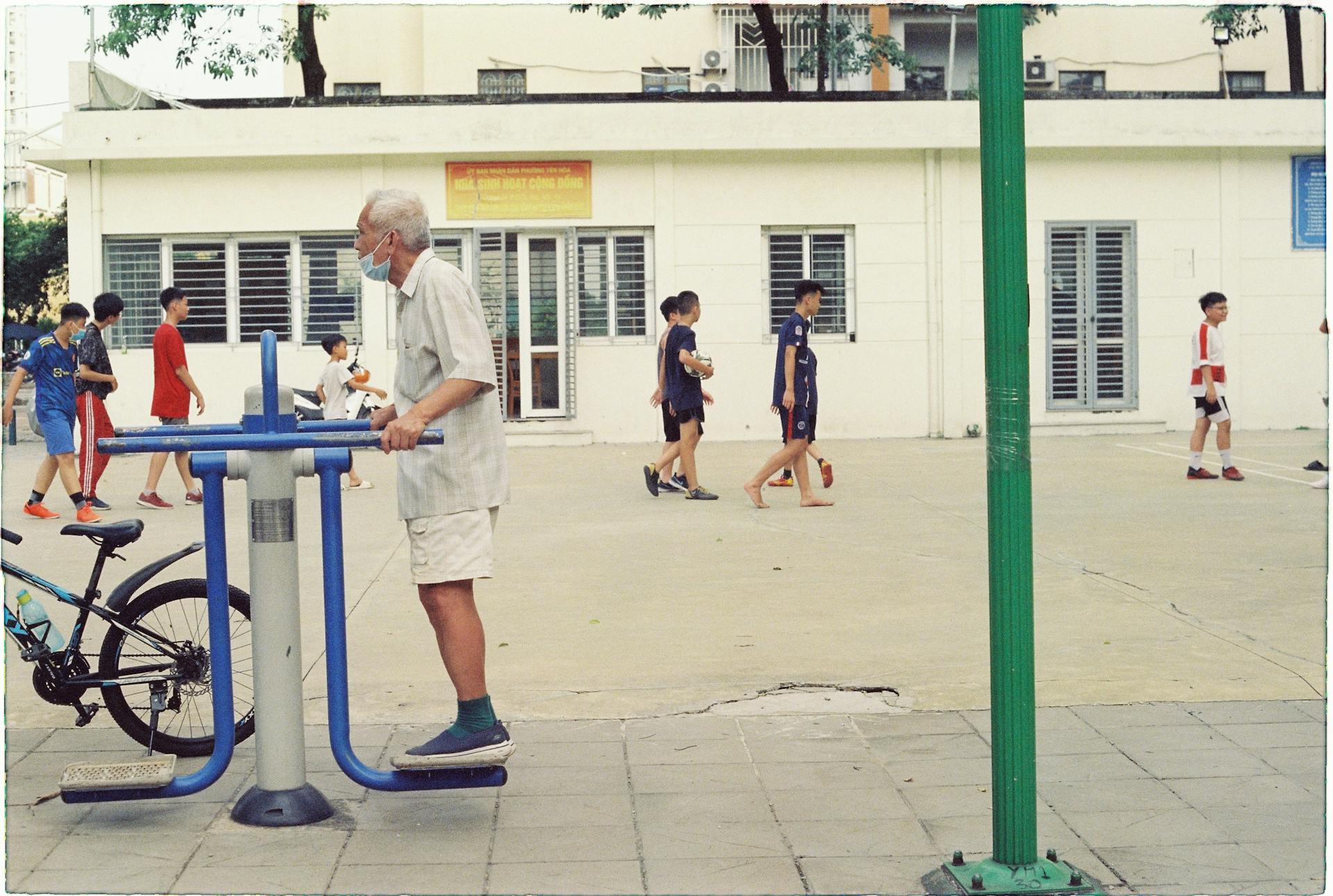 Senior man using exercise equipment in a lively community park with people walking and cycling.