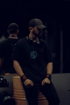 Man in casual gym attire, wearing a cap and headphones, posing in a fitness setting.