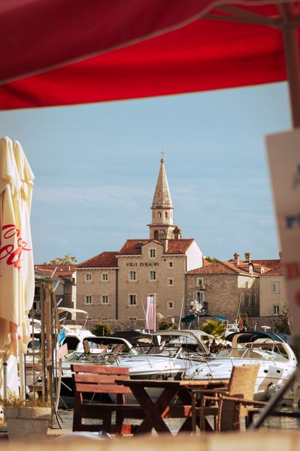 Scenic view of Budva's waterfront with docked boats and historic architecture on a sunny day.