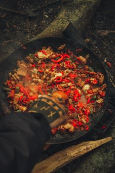 Vibrant outdoor cooking scene with sizzling vegetables and meats in a smoky pan.