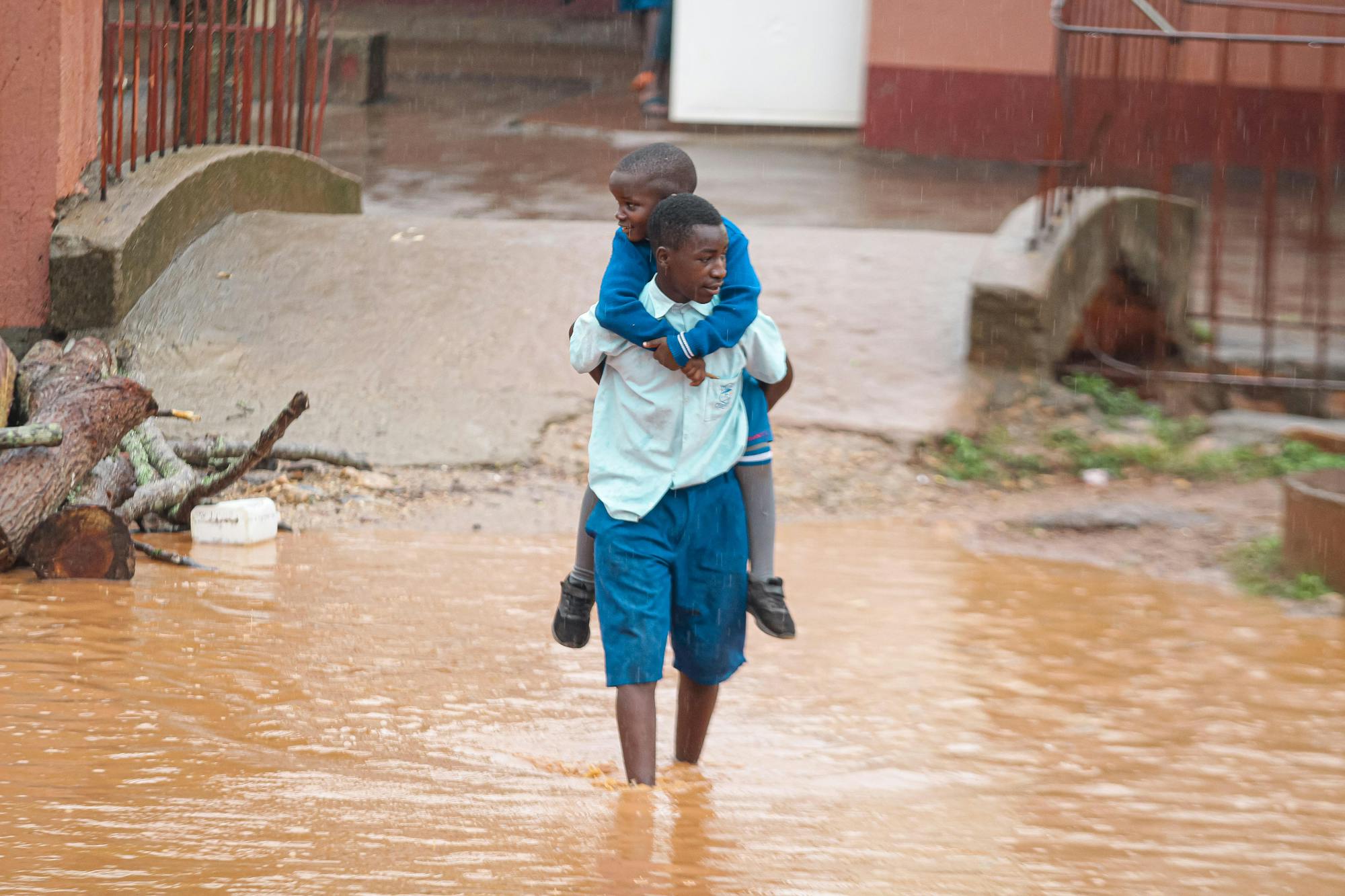 Young Man Carrying a Child Through a Flooded Street
