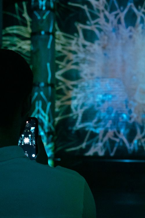 Free A person photographing a vibrant digital art installation using a smartphone at night. Stock Photo