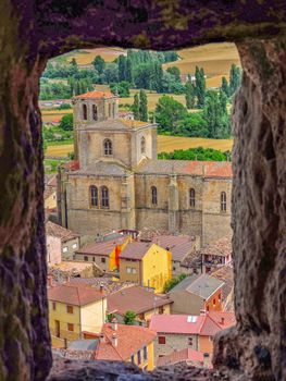 Picturesque view of Peñaranda de Duero through a stone window, featuring rustic architecture and lush countryside.