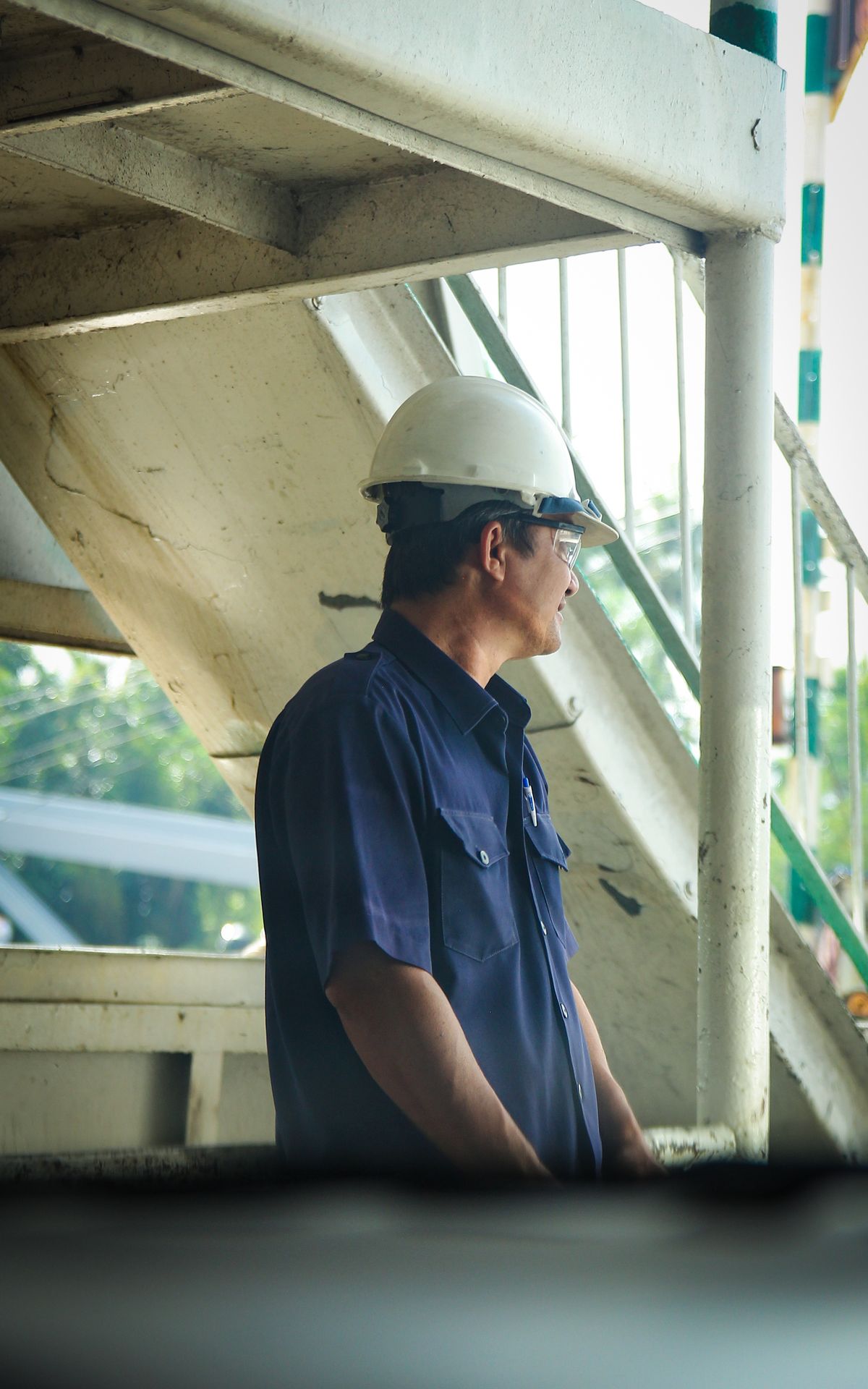 Engineer in protective gear beside industrial steel structure and access stairs during plant maintenance work