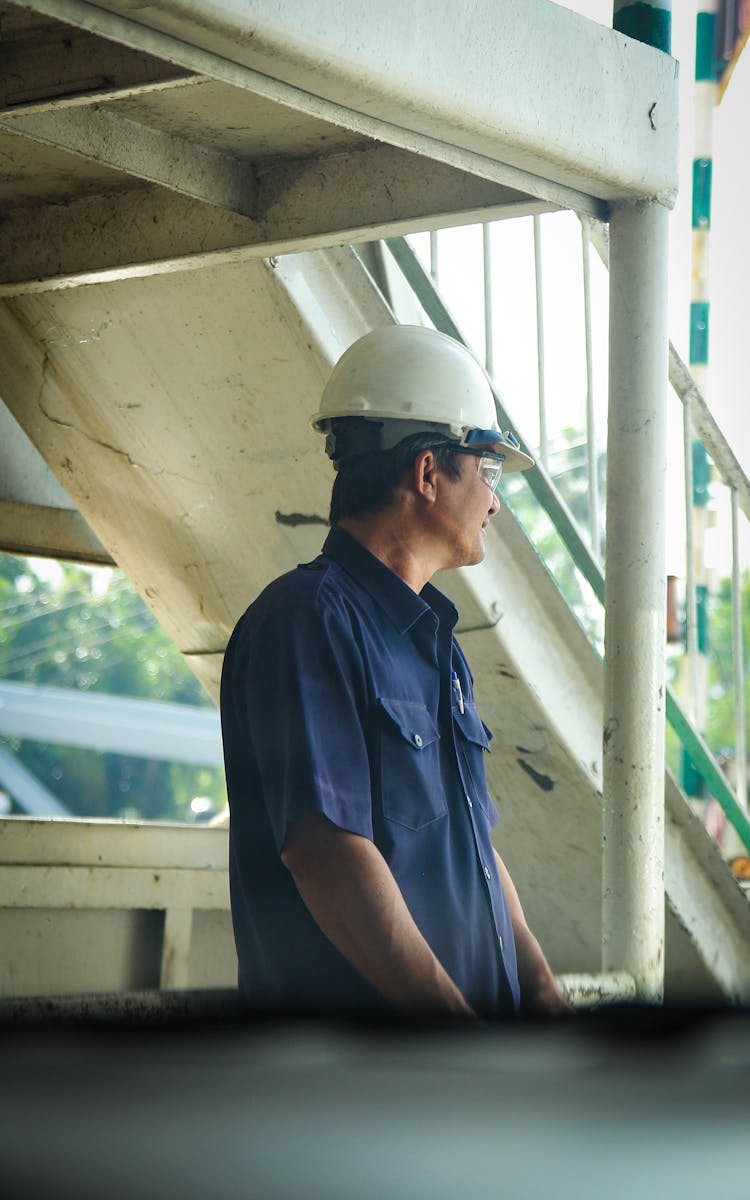 Man In Blue Polo Shirt Wearing A Hardhat Under A Metal Structure