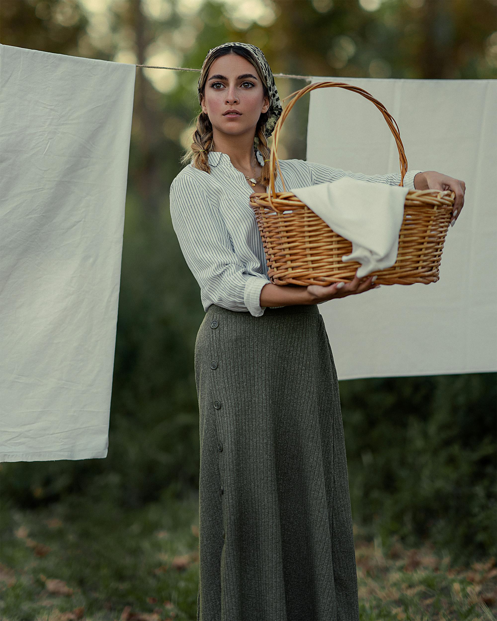 Young woman holding a woven basket with clothes outdoors by a clothesline.