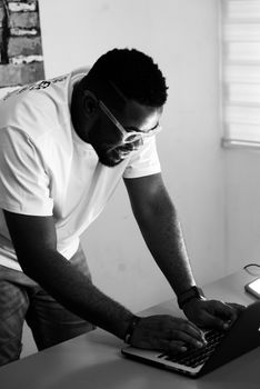 Monochrome image of a man smiling while working on a laptop indoors.