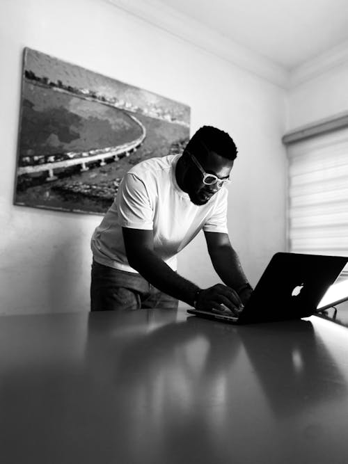 Grayscale Photo of a Man in Black Shirt Using His Laptop