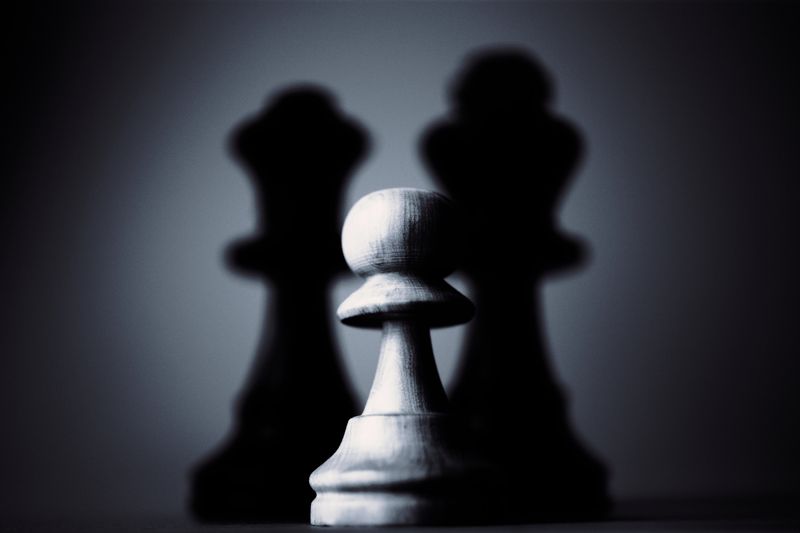 Moody black and white photograph of a chess pawn highlighting strategy and shadow play.