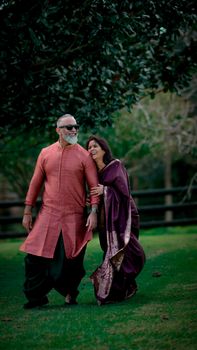An elderly couple enjoying a romantic walk outdoors, dressed in traditional clothing.
