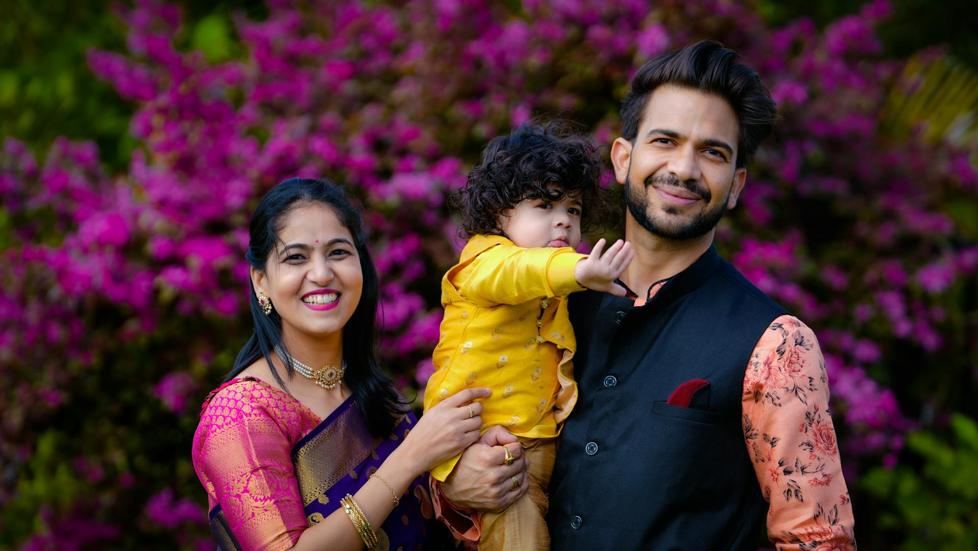 A cheerful Indian family enjoying outdoor time in colorful traditional attire with blooming flowers.