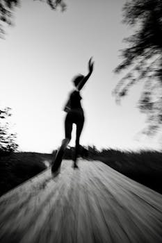 Blurred motion black and white photo of a person running outdoors, conveying speed and movement.