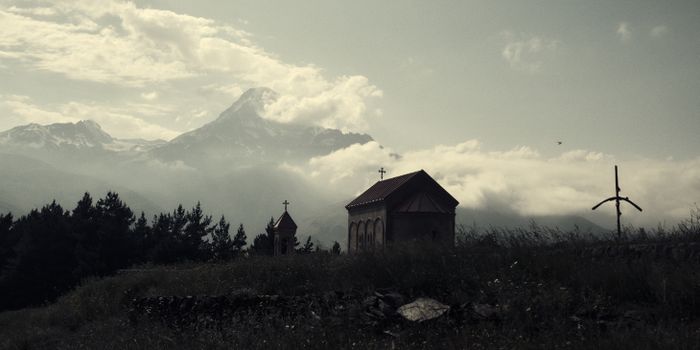 A picturesque chapel with mountains in Stepantsminda, Mtskheta-Mtianeti, Georgia under cloudy skies.