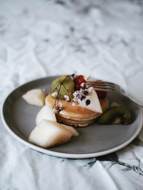 Tasty pancakes topped with fresh fruit slices and flowers on a grey plate.