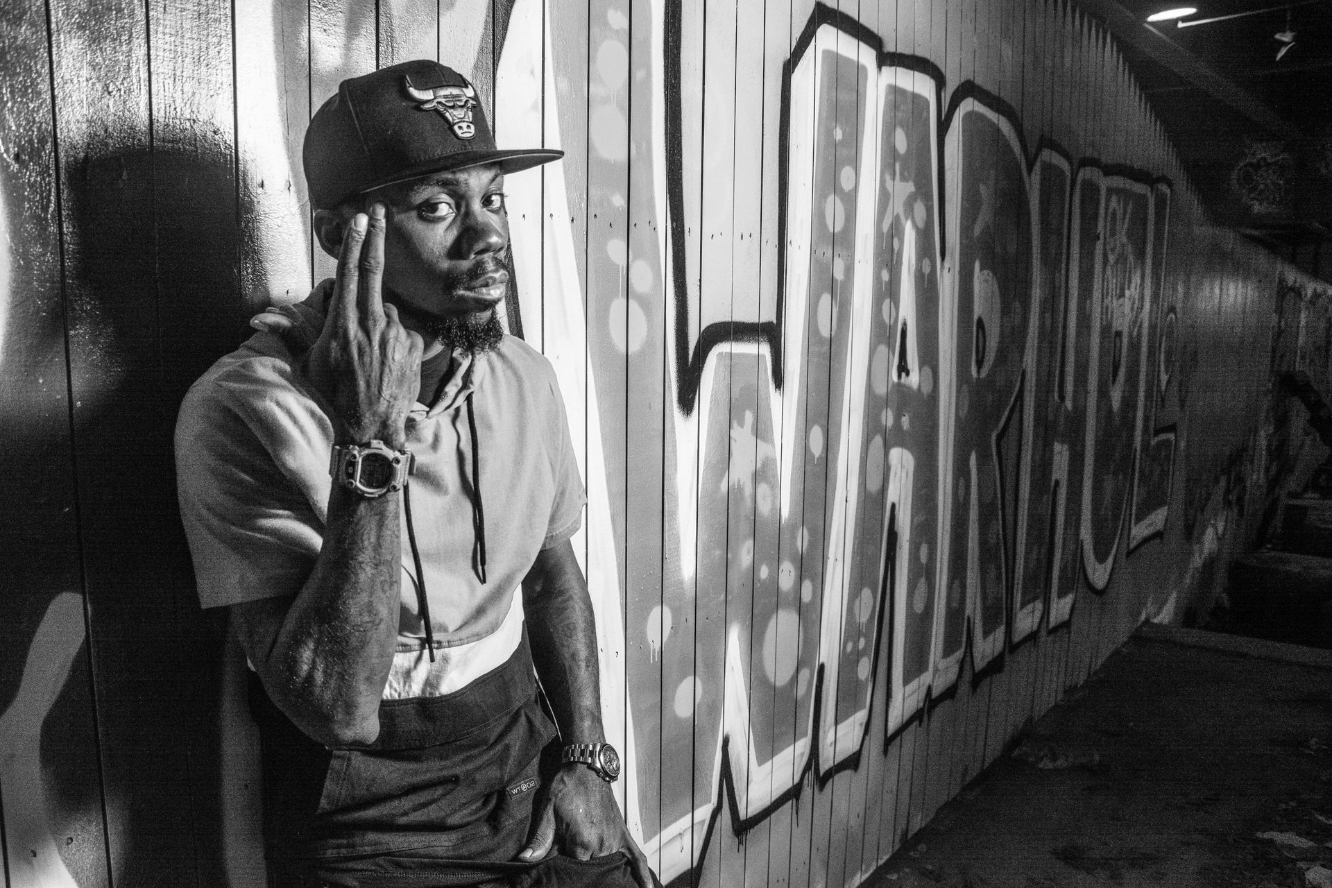 Grayscale Photo of Man Leaning On Wall With Graffiti