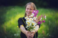 一位女士在户外微笑着，手持一束色彩缤纷的野花，背景是模糊的绿色