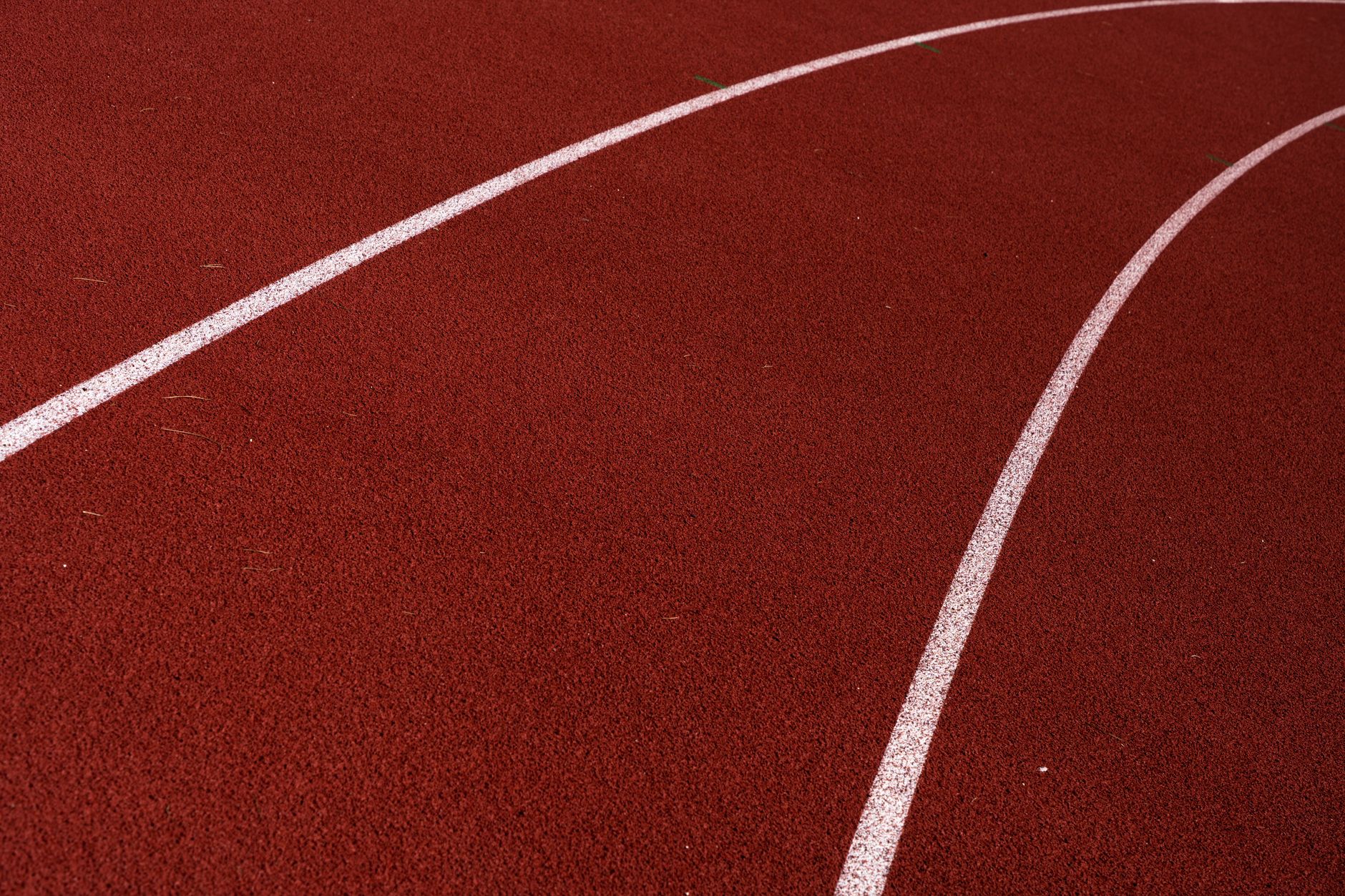 Curved red outdoor running track with white lines and textured surface.